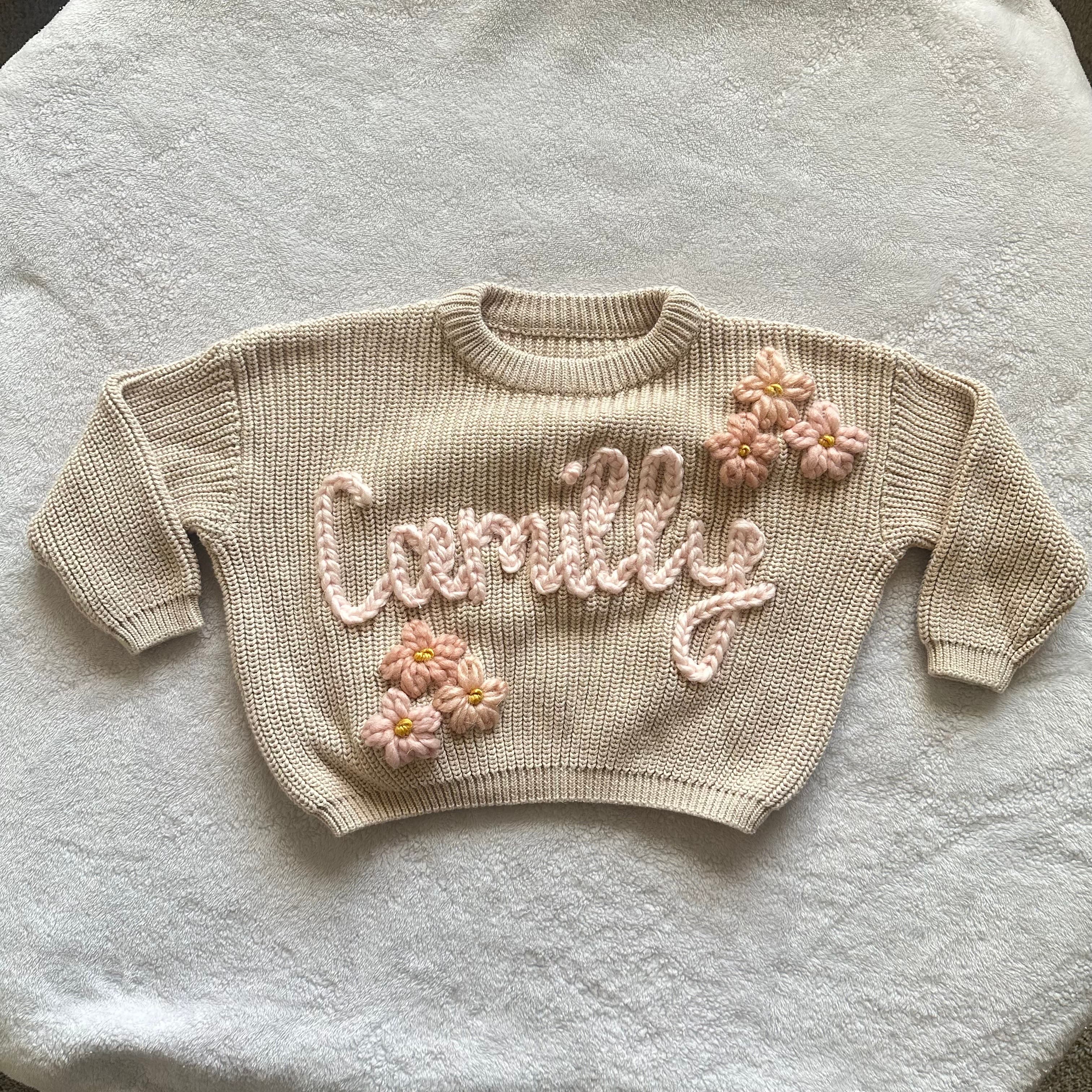Cream sweater stitched with the name Camilly in pink, with crochet flowers