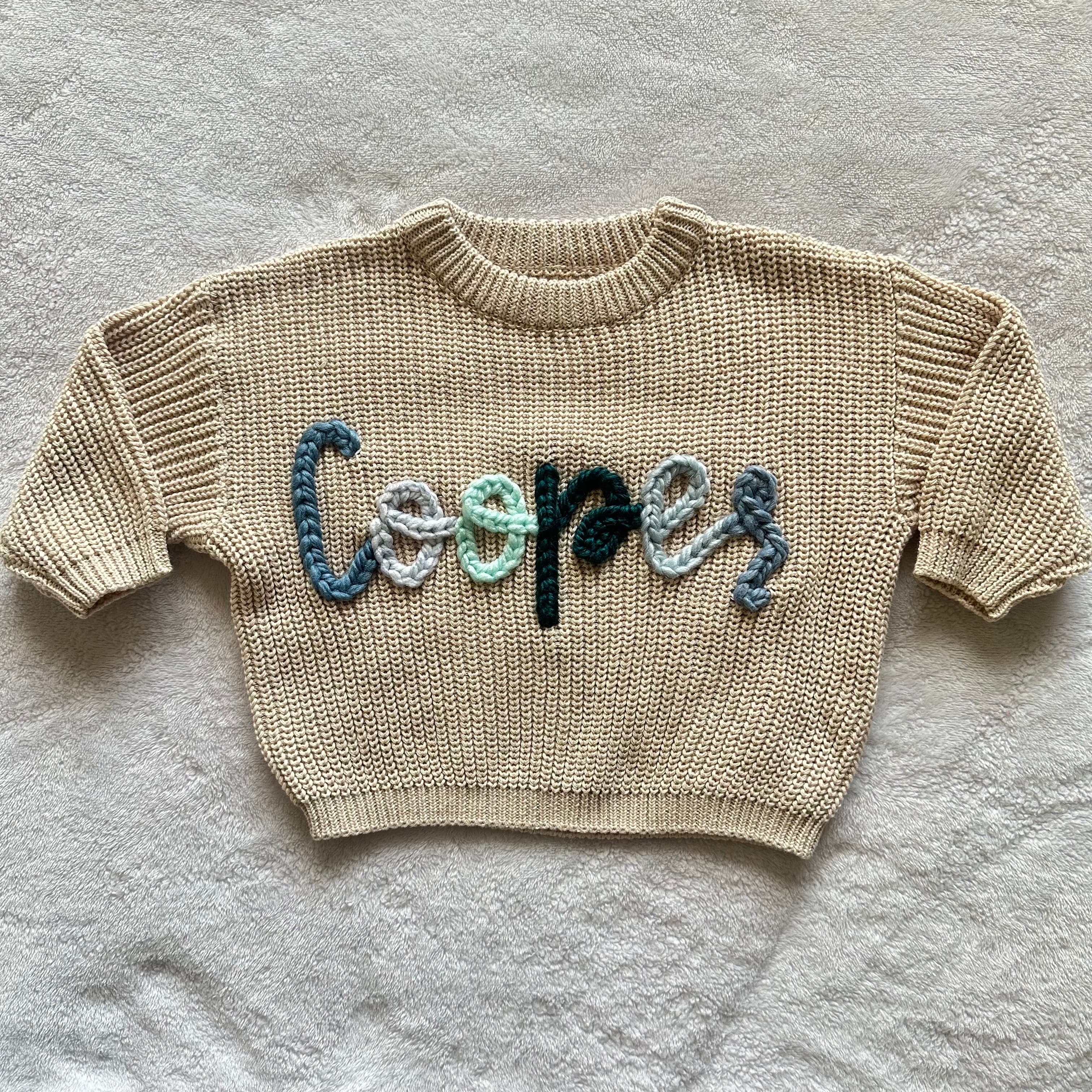 Cream sweater stitched with the name Cooper in blue and green