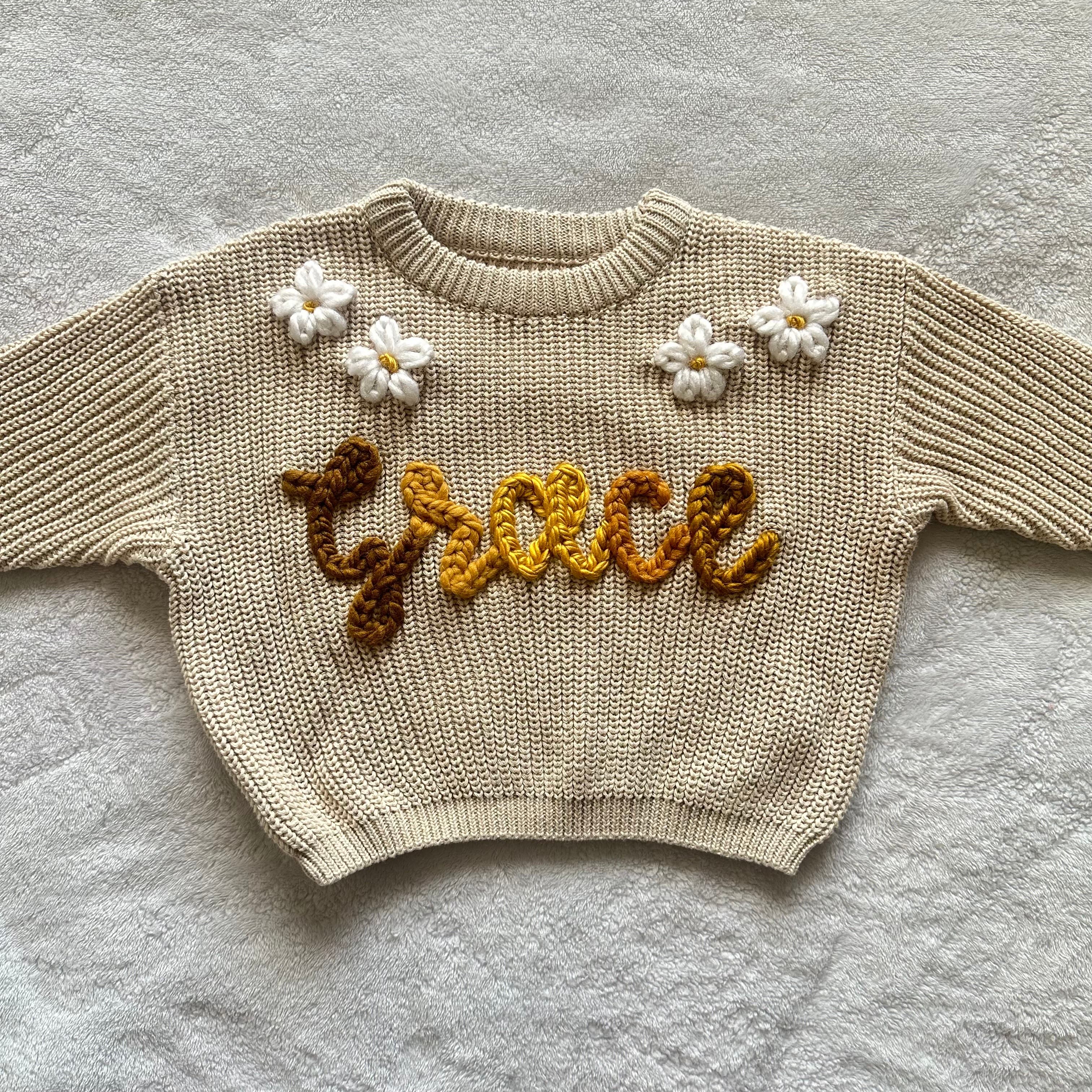 Cream sweater stitched with the name Grace in golden brown, with white flowers