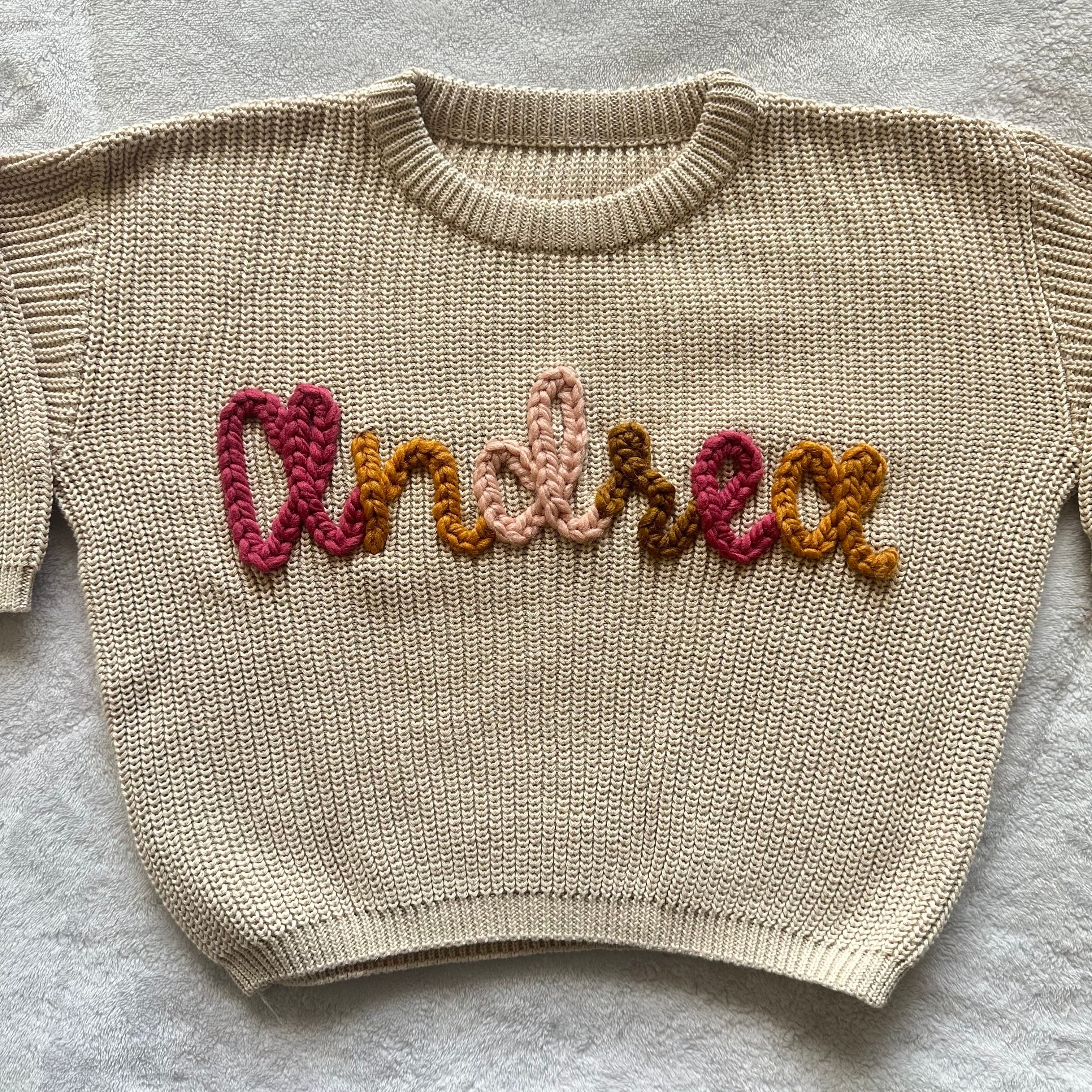 Cream sweater stitched with the name Andrea in a rainbow of warm colors